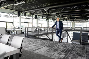 Businessman looking away while standing by railing in office - PESF03178