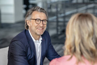 Smiling businessman wearing eyeglasses discussing with female colleague in office - PESF03192