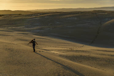 Male tourist carrying tripod while walking on sand during sunset - TOVF00278