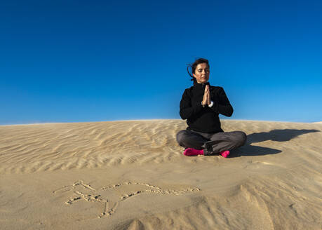 Frau meditiert auf Sand an einem sonnigen Tag - TOVF00279