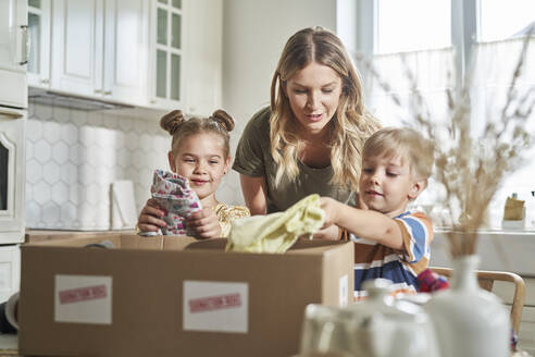 Woman talking with children packing clothes in donation box at home - ABIF01564