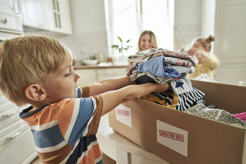 Boy arranging clothes in donation box with family in background - ABIF01566