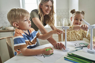 Mutter erklärt Kindern zu Hause das Modell einer Windkraftanlage - ABIF01569