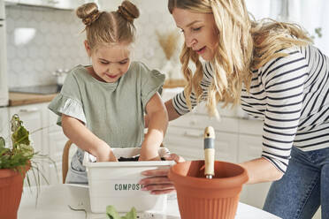 Frau bringt Mädchen bei, wie man zu Hause Kompost in einem Behälter herstellt - ABIF01611