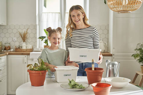 Glückliche Mutter und Tochter mit selbstgebauten Kompostbehältern in der Küche - ABIF01613