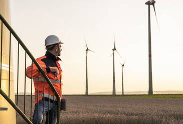 Male inspector at wind turbines during sunset - UUF24601