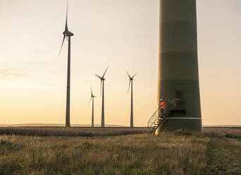 Männlicher Ingenieur an der Treppe der Windkraftanlage bei Sonnenuntergang - UUF24603