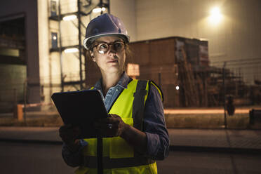 Nachdenkliche Ingenieurin mit digitalem Tablett vor einer Industrie - UUF24607