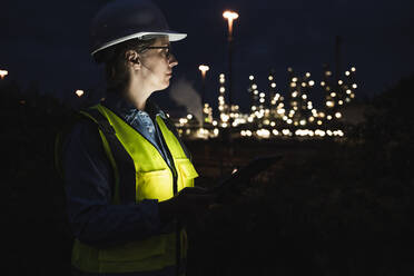 Ingenieurin mit Schutzhelm und reflektierender Kleidung in einer Fabrik bei Nacht - UUF24612