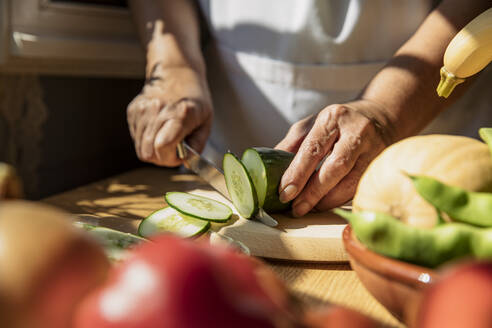 Senior woman cutting cucumber in kitchen - ACPF01299