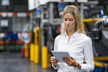 Blonde Geschäftsfrau mit digitalem Tablet in einer Fabrik - DIGF16395