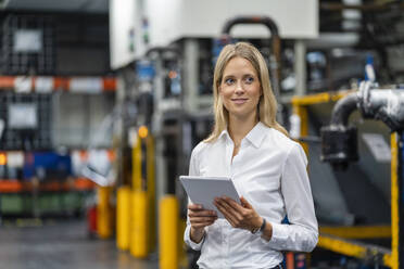 Lächelnde Geschäftsfrau mit digitalem Tablet in einer Fabrik stehend - DIGF16396