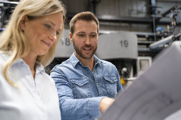 Männlicher Fachmann erklärt einer Kollegin den Plan in einer Fabrik - DIGF16418