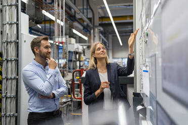 Businesswoman explaining colleague over whiteboard in factory - DIGF16432