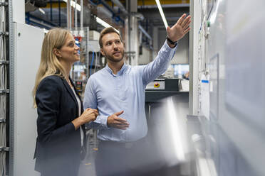 Businessman pointing at whiteboard while explaining female manager in industry - DIGF16433