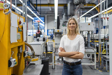 Weibliche Fachkraft mit verschränkten Armen an einer Maschine in einer Fabrik stehend - DIGF16437