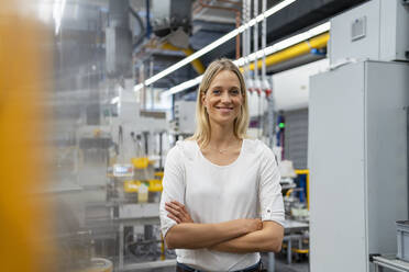 Happy businesswoman standing with arms crossed at industry - DIGF16438