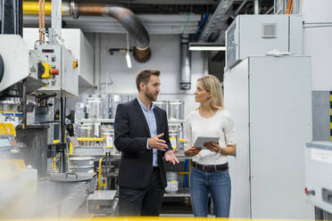 Businesswoman with digital tablet listening to manager while standing in factory - DIGF16444