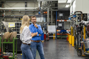 Weibliche Fachkraft im Gespräch mit einem männlichen Mitarbeiter in einer Fabrik - DIGF16461