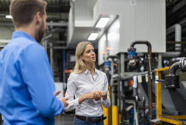 Businesswoman checking machine while standing with coworker in factory - DIGF16463