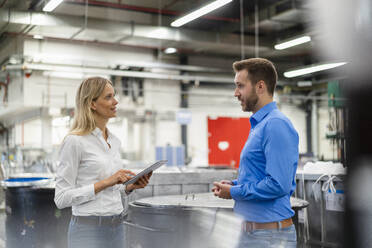 Young businesswoman holding digital tablet while discussing with colleague in factory - DIGF16473