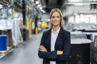 Young businesswoman with arms crossed standing at industry - DIGF16476