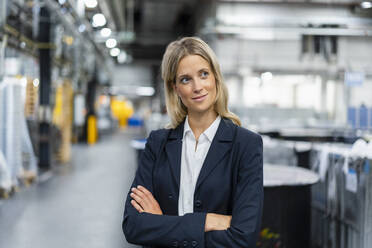 Thoughtful female manager with arms crossed in factory - DIGF16479