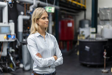 Thoughtful businesswoman with arms crossed in factory - DIGF16502