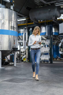Junge Geschäftsfrau, die beim Gehen in einer Fabrik ein digitales Tablet benutzt - DIGF16503