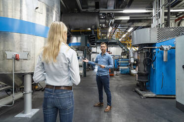 Geschäftsmann, der auf eine Fertigungsmaschine zeigt, während er mit einem Kollegen in einer Fabrik arbeitet - DIGF16511