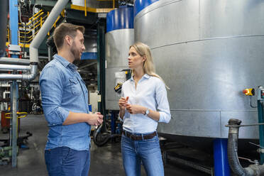 Male and female coworkers discussing while standing in factory - DIGF16513