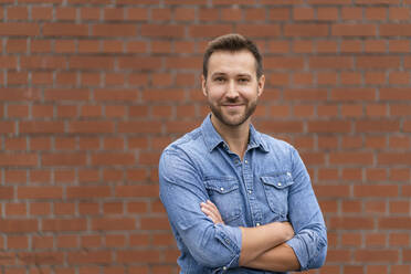 Happy businessman with arms crossed in front of wall - DIGF16533