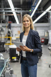 Blonde Geschäftsfrau mit digitalem Tablet in einer Fabrik stehend - DIGF16537