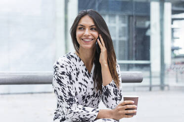 Lächelnde Frau, die mit ihrem Smartphone telefoniert, während sie Kaffee trinkt - PNAF02192