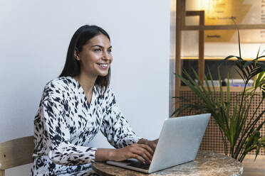 Smiling female freelancer working on laptop at coffee shop - PNAF02206