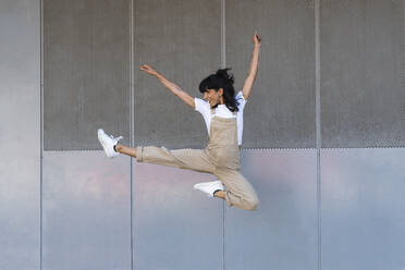 Carefree woman jumping in front of metal wall - PNAF02237