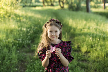 Nettes Mädchen hält ein Pfingstrosenblatt, während sie auf einer Wiese steht - LLUF00013