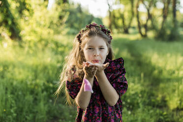 Playful girl with flower tiara blowing peony petal - LLUF00014