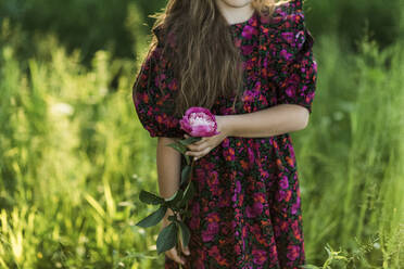 Girl holding peony flower while standing on meadow - LLUF00022