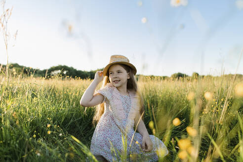 Lächelndes Mädchen hält Hut, während es auf einer Wiese kniet - LLUF00023