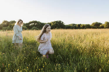 Playful girl and woman running at meadow during sunset - LLUF00026