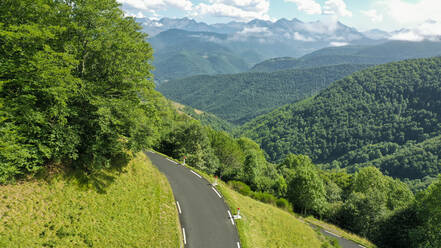 Luftaufnahme einer Bergstraße und eines grünen, bewaldeten Tals - OCAF00737