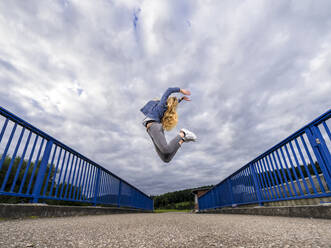 Junge Frau springt gegen den bewölkten Himmel über die Remsbrucker Brücke - STSF03033