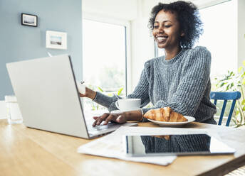 Smiling female freelancer using laptop during video conference at home office - UUF24616