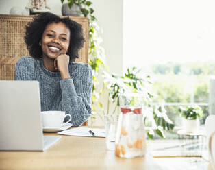 Young businesswoman with hand on chin smiling at desk - UUF24619