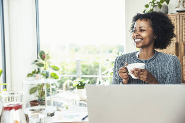 Young businesswoman smiling while having coffee at home - UUF24620