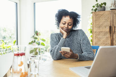 Afro female freelancer using smart phone at home office - UUF24624