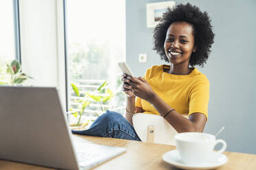 Female freelancer holding smart phone at home office - UUF24629