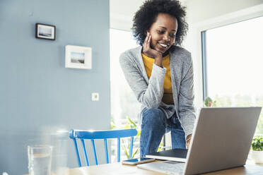 Smiling businesswoman using laptop while leaning on chair at desk - UUF24640