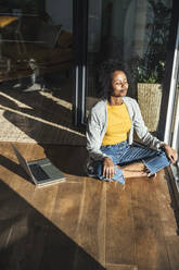 Woman with eyes closed meditating while sitting on floor at home - UUF24685